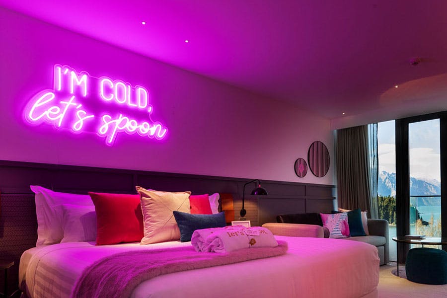 pink neon sign over bed reading I'm cold let's spoon
