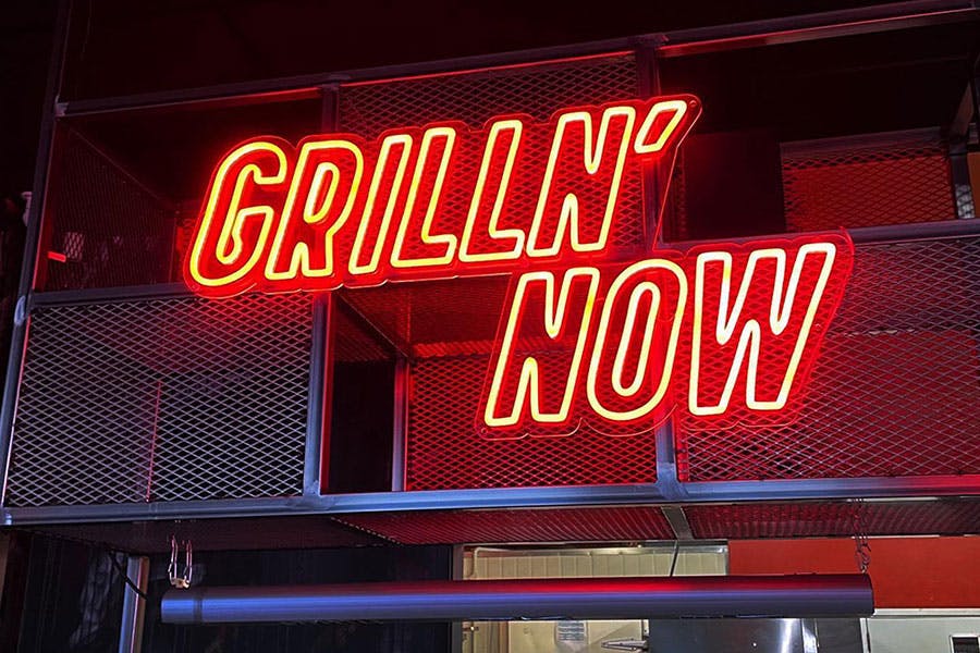 red neon sign reading grilln' now over grill