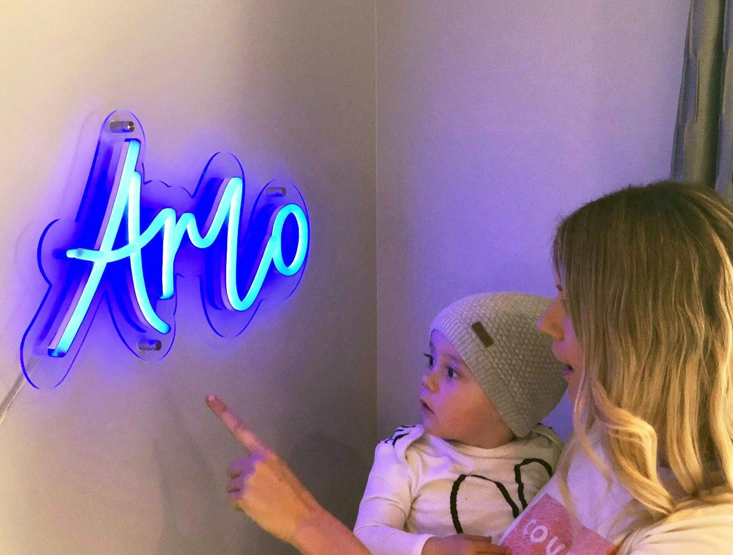 a person with a baby pointing at an ‘Arlo’ neon sign
