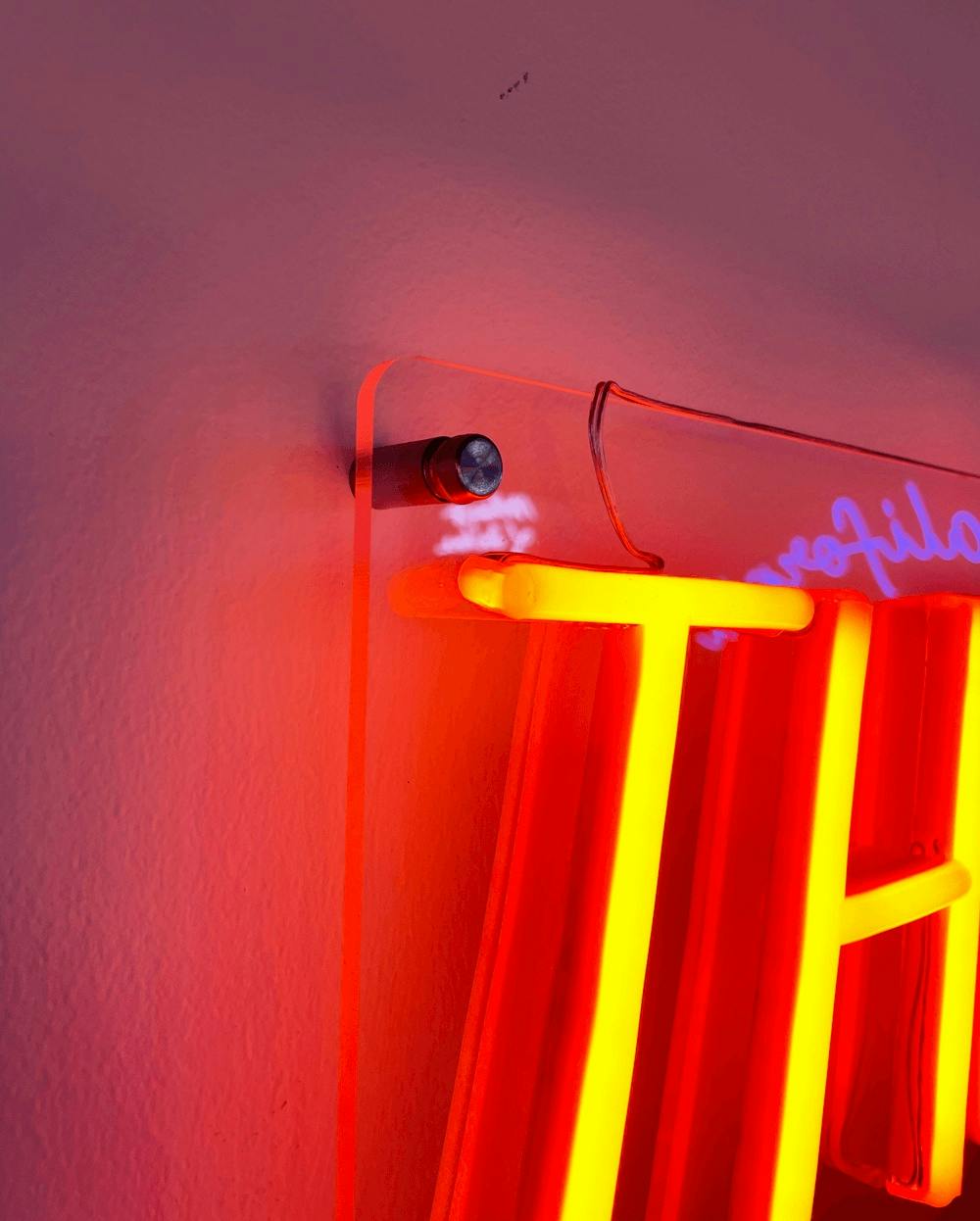 a yellow neon sign hanging with a stand-off screw